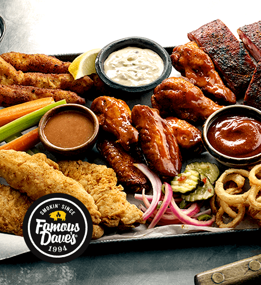 Famous Dave's BBQ platter with chicken wings, roasted chicken, breaded chicken strips, ribs, pickles, pickled onions, celery and carrot sticks, and various dipping sauces