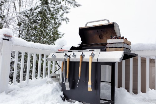 Snow covers a porch with a barbeque's lid open, ready for some winter grilling.