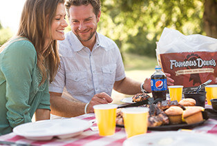 A couple eating Famous Dave's BBQ at a picnic table outside