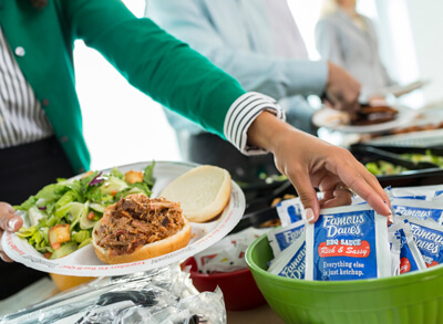 A woman grabbing a Famous Dave's sauce packet for her food catered by Famous Dave's