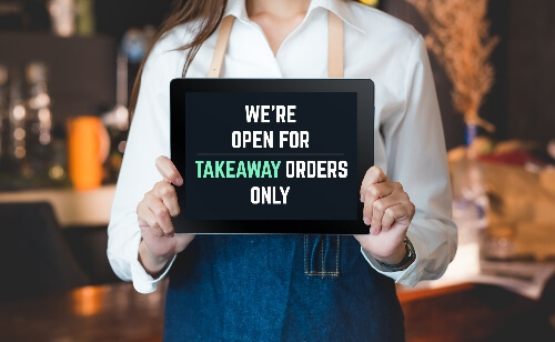 A server holds a sign that reads "we're open for takeaway orders only." 