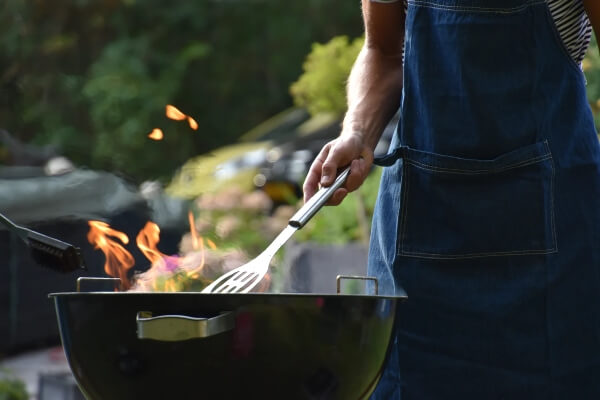 A man stands in front of a grill, tending to his barbeque meats.