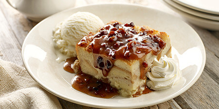 Dave's Award-Winning Bread Pudding on a white plate, topped with a golden brown pecan praline sauce, with a scoop of vanilla ice cream on the side