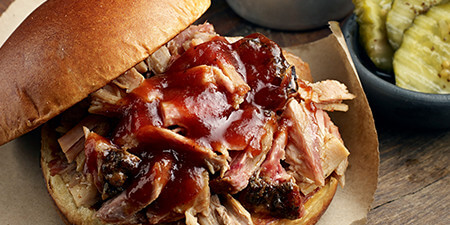 Image of a chopped pork sandwich in a hamburger bun, smothered with BBQ sauce