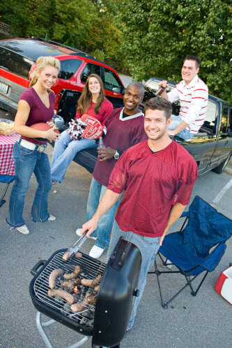 Some young people have a tailgating party going with BBQ food cooking on the grill.