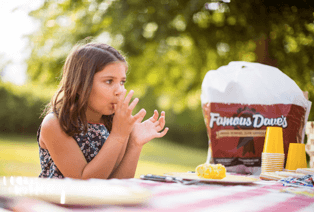 Girl eating Famous Dave's BBQ licking fingers at a picnic table.